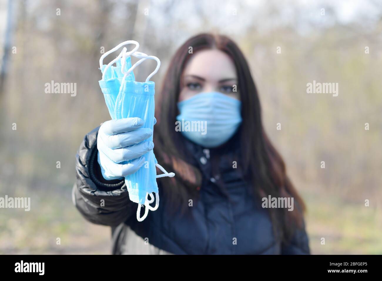 La jeune femme dans le masque de protection montre un groupe de masques de protection bleus à l'extérieur dans le bois de printemps. Concept d'utilisation de produits de protection pendant la quarantaine Banque D'Images