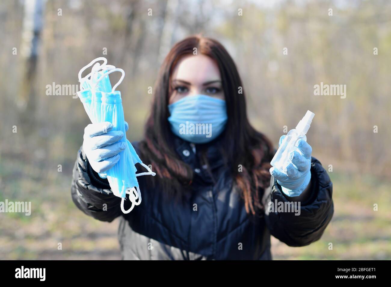 La jeune femme présente dans un masque de protection des bouteilles de vaporisation désinfectante et des masques de protection extérieurs en bois de printemps. Concept d'utilisation de produits antibactériens d Banque D'Images