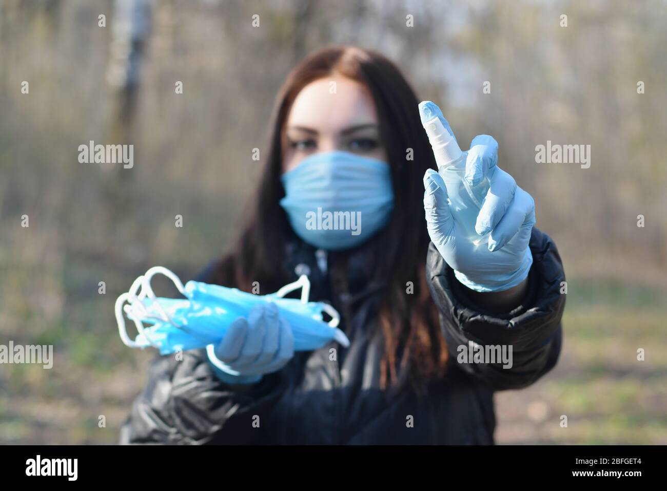 La jeune femme présente dans un masque de protection des bouteilles de vaporisation désinfectante et des masques de protection extérieurs en bois de printemps. Concept d'utilisation de produits antibactériens d Banque D'Images