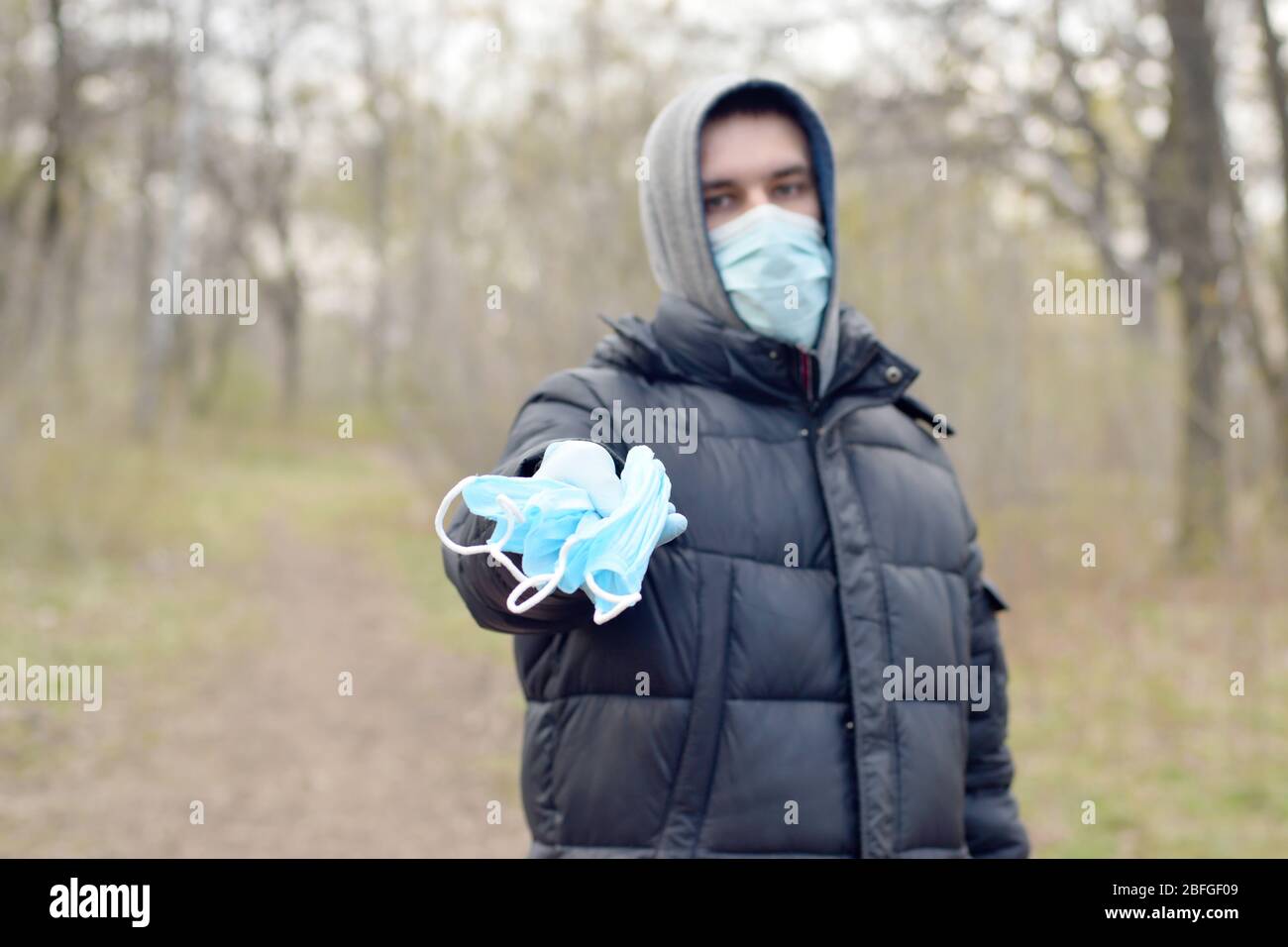 Le jeune homme dans le masque de protection montre un groupe de masques de protection du visage à l'extérieur dans le bois de printemps. Concept d'utilisation de produits de protection pendant la quarantaine Banque D'Images