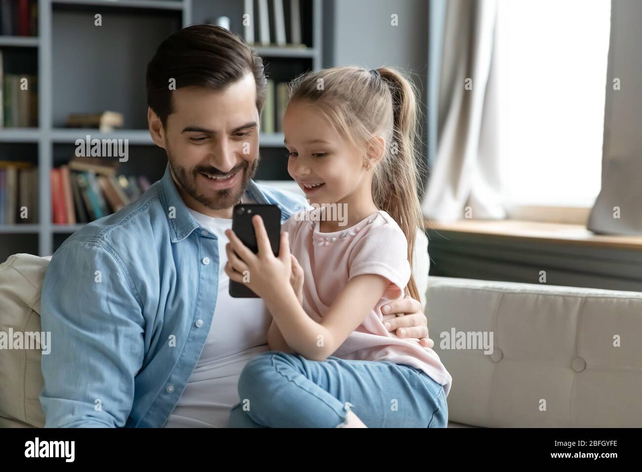 Petite fille montrant à père nouveau jeu cool sur smartphone Banque D'Images