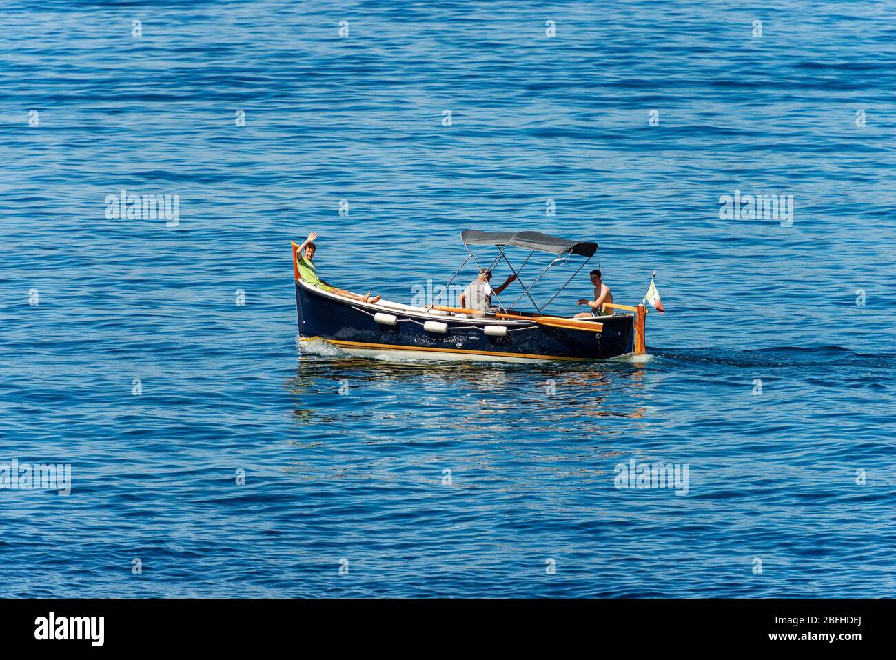 Petit bateau à moteur en bois avec trois personnes à bord, deux adolescents et un homme âgé en mouvement dans la mer Méditerranée, Ligurie, Italie, Europe Banque D'Images