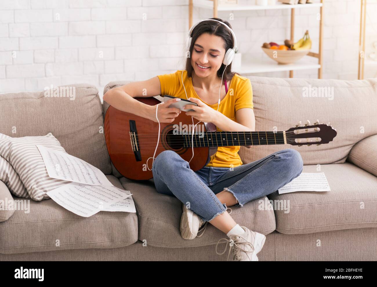 Restez à la maison. Bonne fille dans un casque avec guitare acoustique  prenant la classe de musique en ligne via smartphone Photo Stock - Alamy