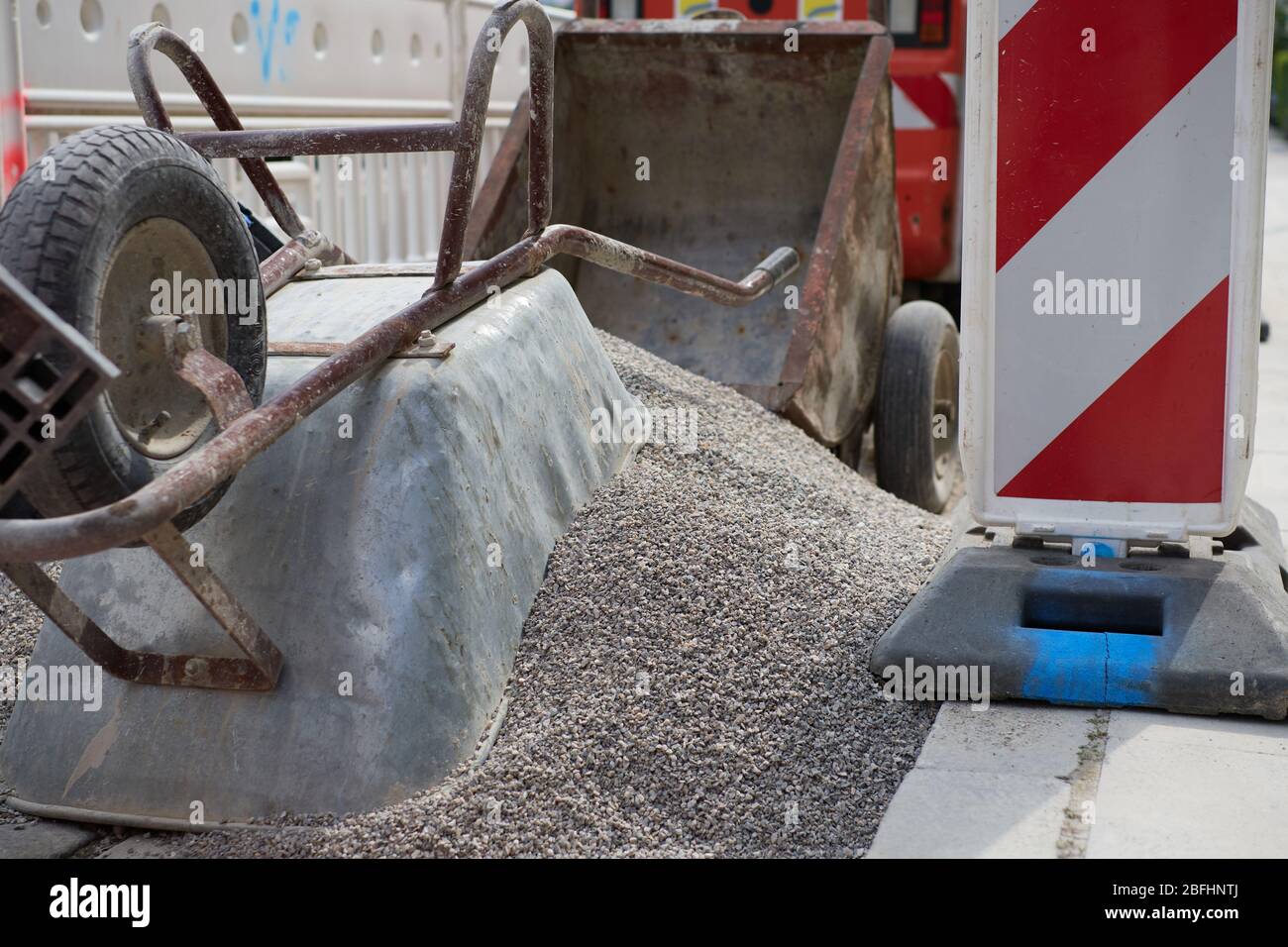 Une brouette sur un tas de gravier sur un chantier dans une ville délimitée par des marquages de sécurité. Concept pour le chantier urbain, lourd dut Banque D'Images