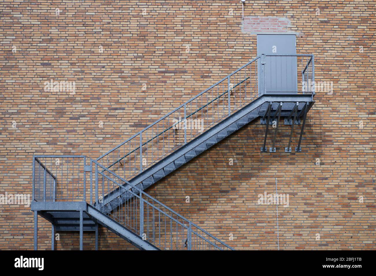 Escalier extérieur en acier menant à une porte fermée sur un mur de bâtiment en brique rouge. Concept pour la construction et l'industrie, la structure et l'architecture, cli Banque D'Images