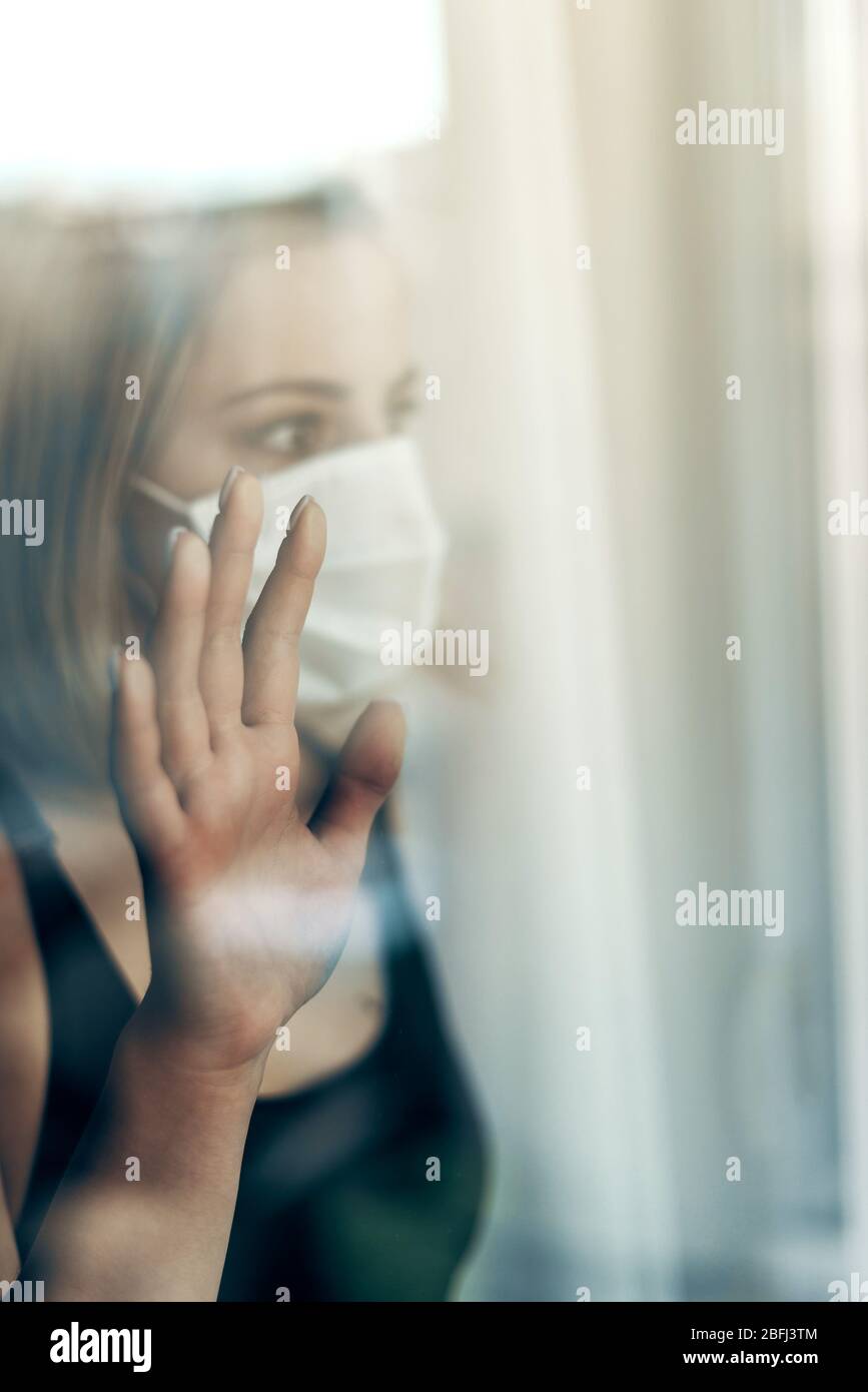 Femme portant protection masque chirurgical regardant par la vitre tout en étant en quarantaine à domicile pendant le virus corona - surnombre de pandémies de covid-19 Banque D'Images