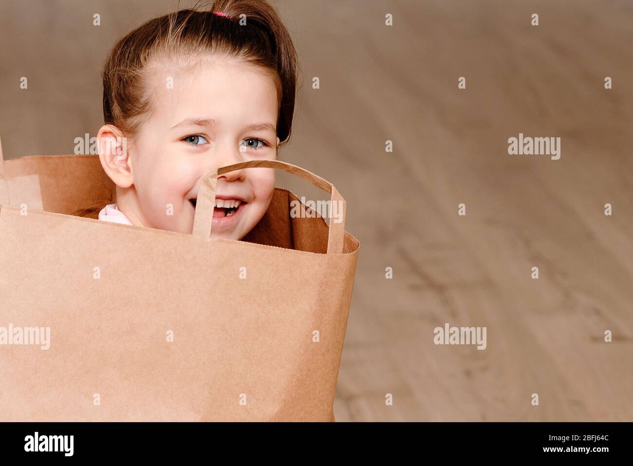 Petite fille assise dans le sac de papier marron, jouant le concept enfants avec espace de copie Banque D'Images