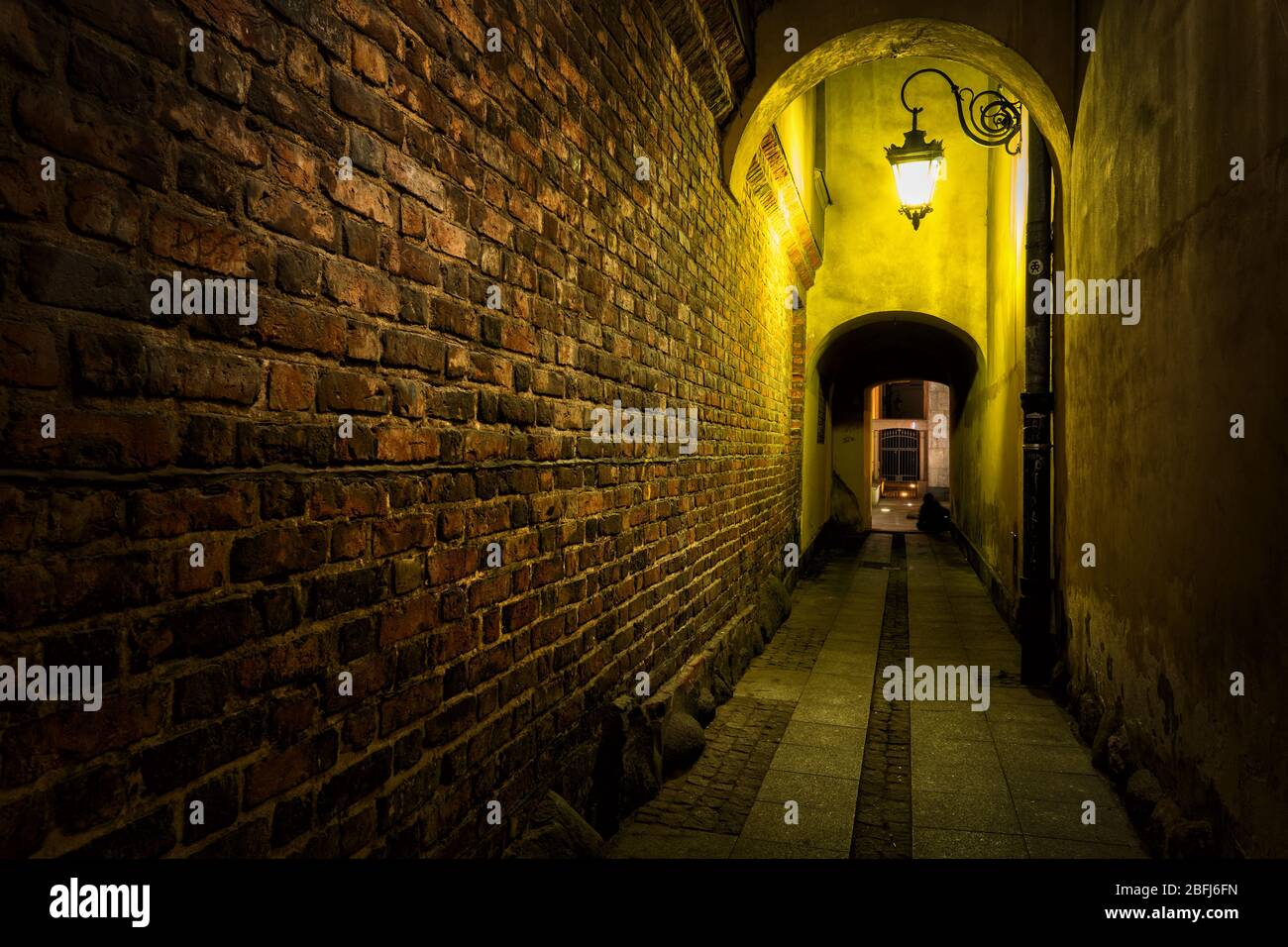 Allée étroite avec mur en briques vieilli illuminé par une seule lampe dans la vieille ville de Varsovie en Pologne. Banque D'Images