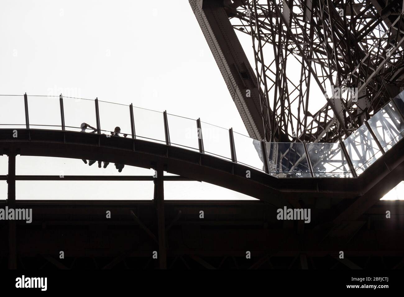Silhouettes de deux personnes se penchant contre une barrière sur la plateforme transparente au premier étage de la Eiffel, vu du dessous, Paris Banque D'Images