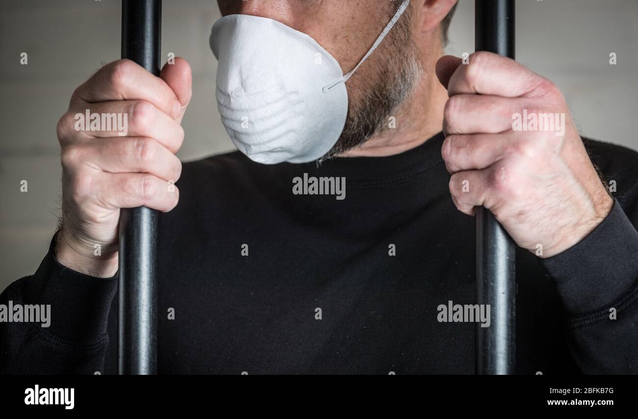 Un prisonnier derrière des barreaux portant un masque pour illustrer les problèmes de Coronavirus et de Covid 19 en prison. Photo posée par le modèle. Banque D'Images