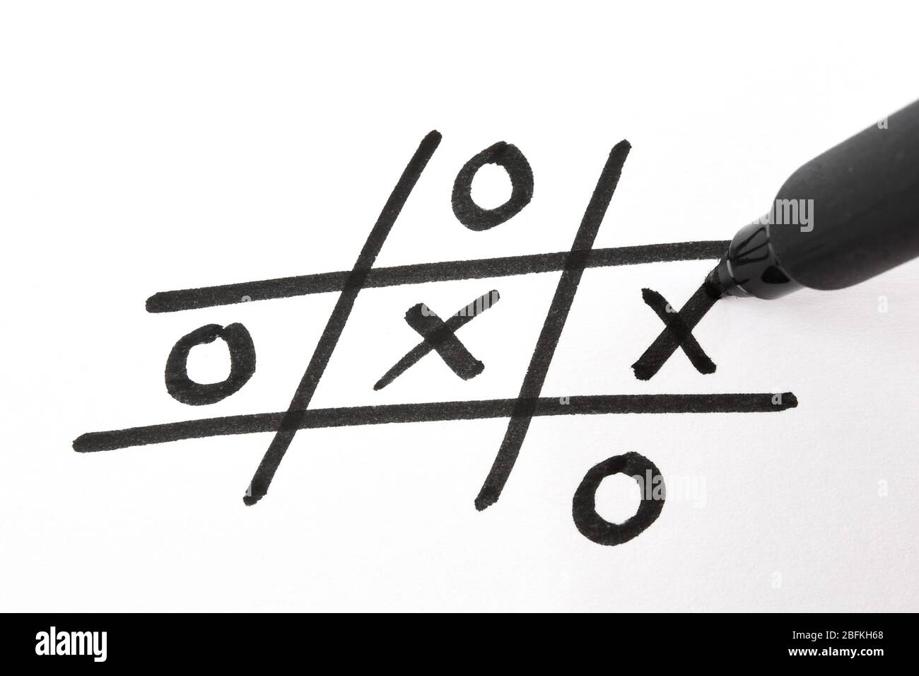 Vue rapprochée d'un stylo à pointe en fibre noire qui écrit un « X » dans un jeu de creux et de croix sur papier blanc Banque D'Images