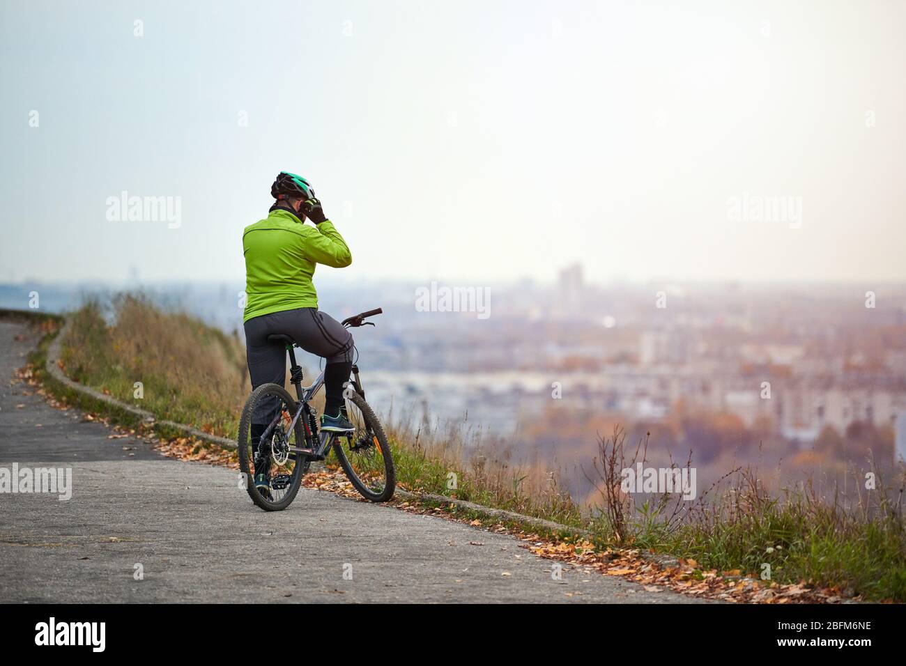 Cycliste en haut de la colline en regardant le paysage urbain, vue arrière,  espace de copie. Peu de pause lors d'une promenade en vélo dans le parc de  la ville d'automne. L'homme