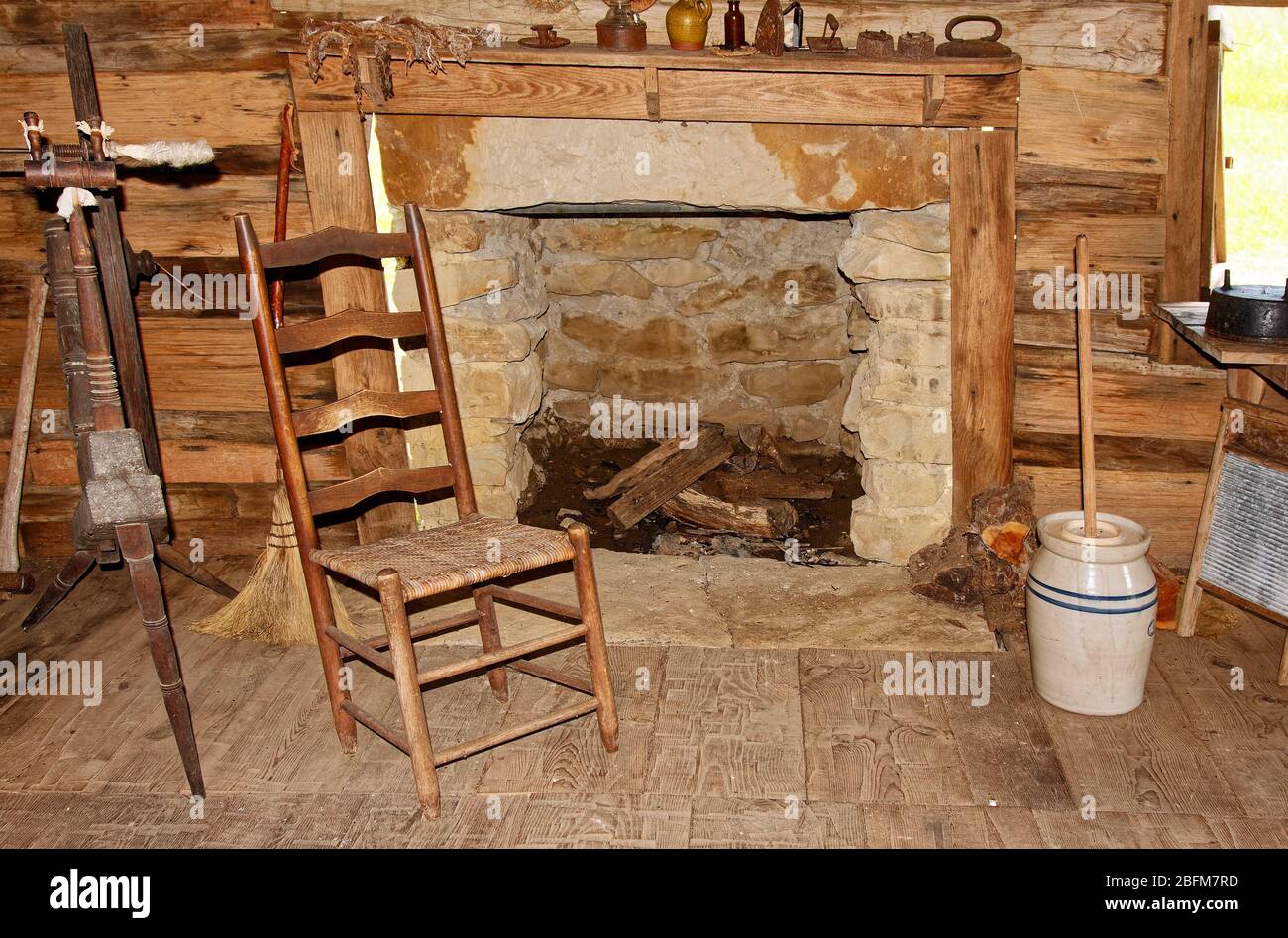 Foyer en brique, intérieur de la vieille cabine en rondins, chaise de siège en rotin, instruments anciens, planche à laver, urne de beurre en céramique, enrouleur de fil, colonie de Hensley; Cumberlan Banque D'Images