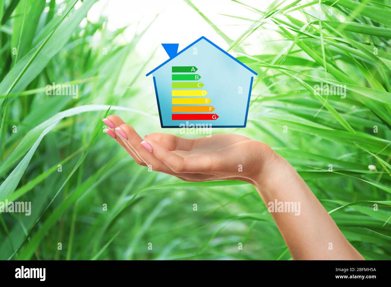 Main et maison de femme avec l'échelle d'efficacité énergétique sur fond naturel Banque D'Images