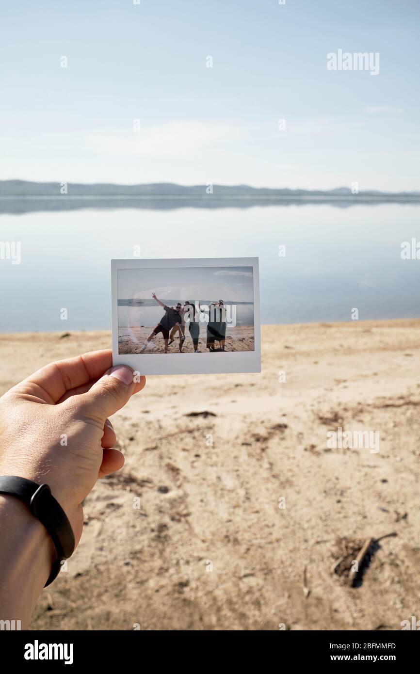 Main masculine tenant la photo poloïde avec groupe de jeunes posant contre le beau lac sur l'été lumineux après-midi Banque D'Images