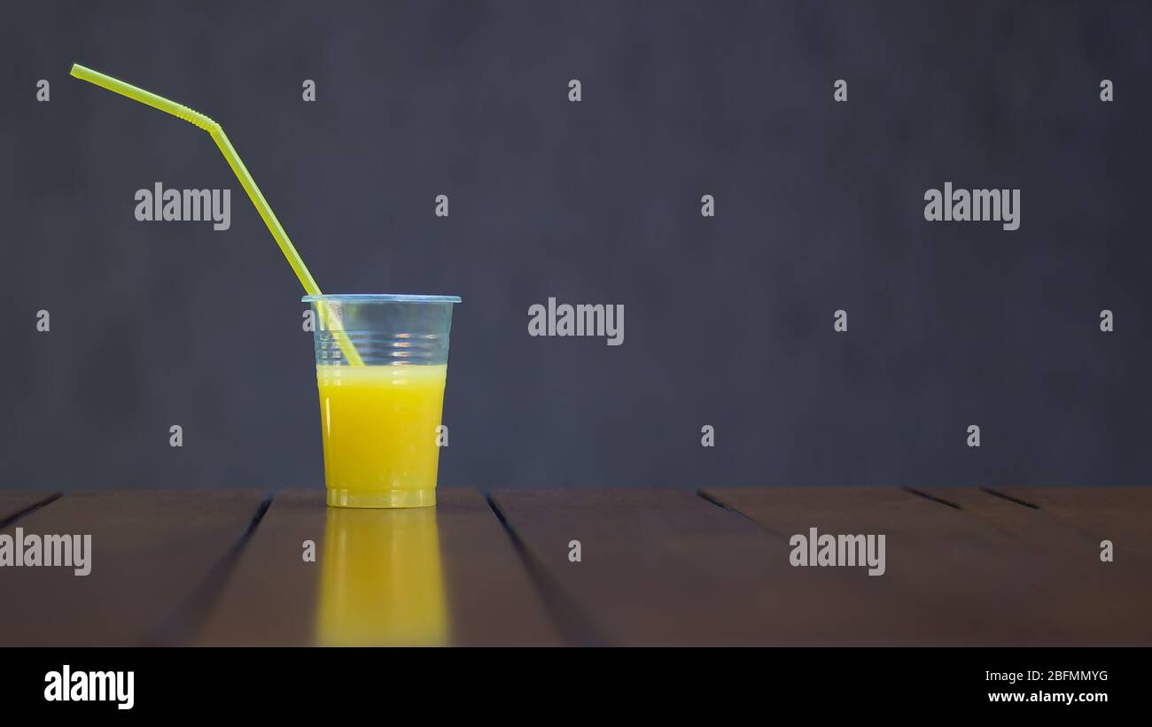 Jus d'orange dans une tasse en plastique avec un tube sur fond brun. Espace de copie. Pique-nique, végétalien, nourriture saine, boisson. Réutilisation et recyclage de pla de qualité alimentaire Banque D'Images