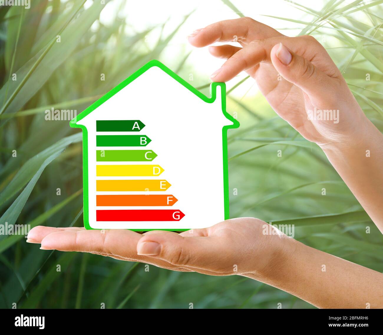 Les mains féminines tiennent la maison avec l'image de l'échelle d'efficacité énergétique sur fond naturel Banque D'Images
