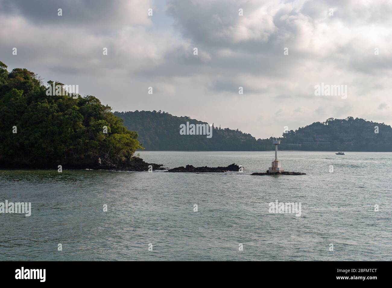 Un petit phare blanc sur les pierres près de l'île sur la rivière. Un petit bateau est visible à la distance. Sur les pistes des maisons de montagne... Banque D'Images