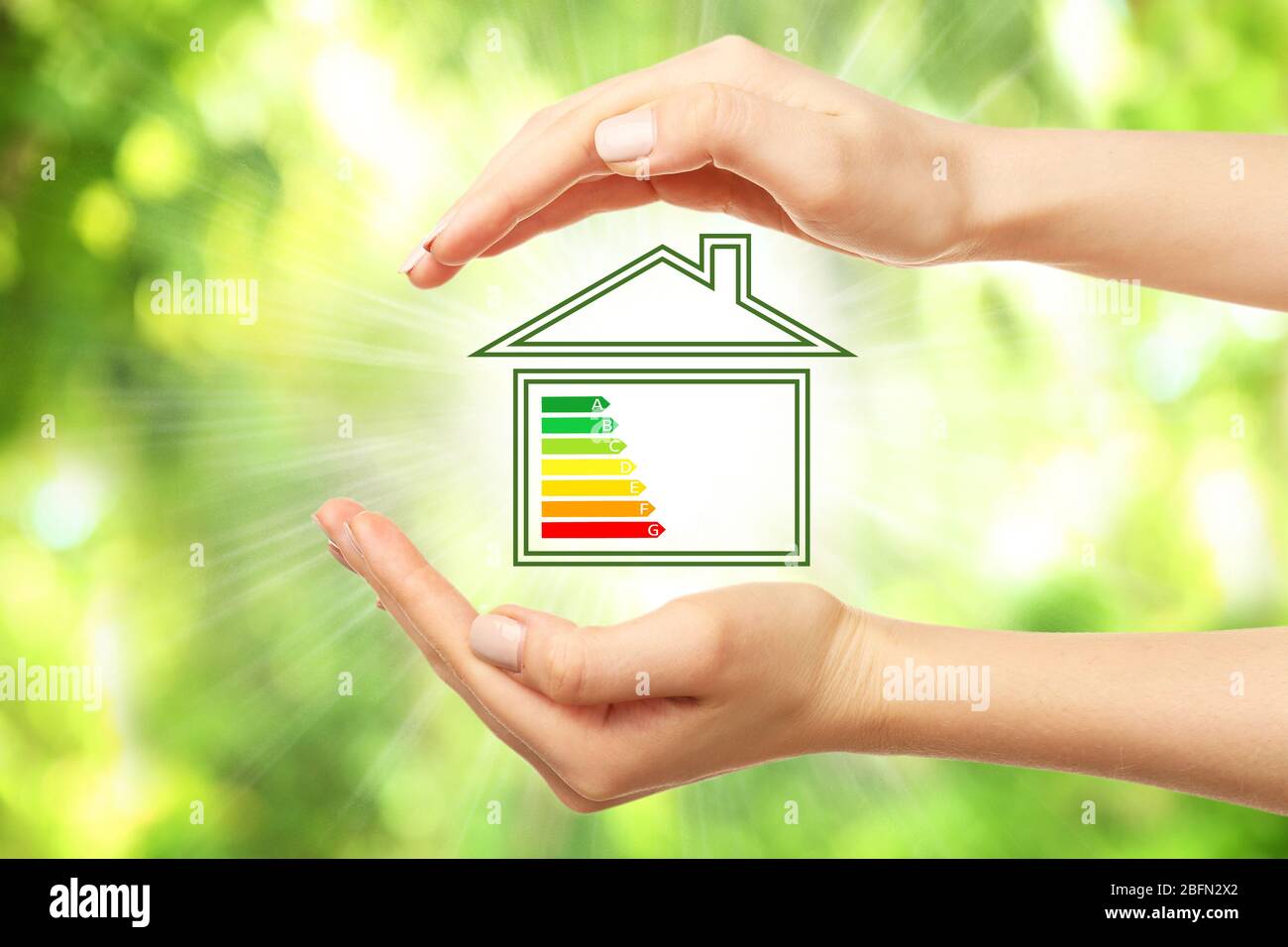 Mains et maison féminines avec l'échelle d'efficacité énergétique sur fond naturel Banque D'Images