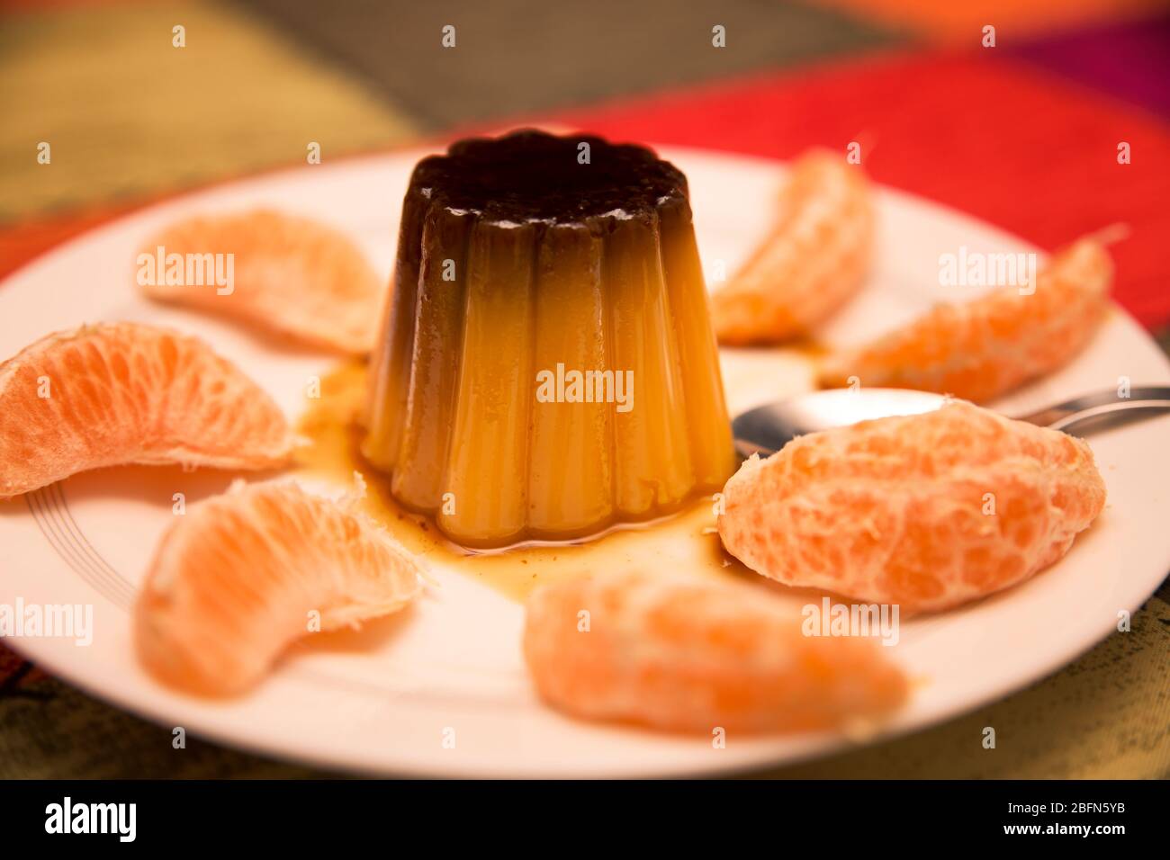 crème anglaise à la vanille et au caramel entourée de segments de mandarine dans un plat blanc sur fond multicolore Banque D'Images