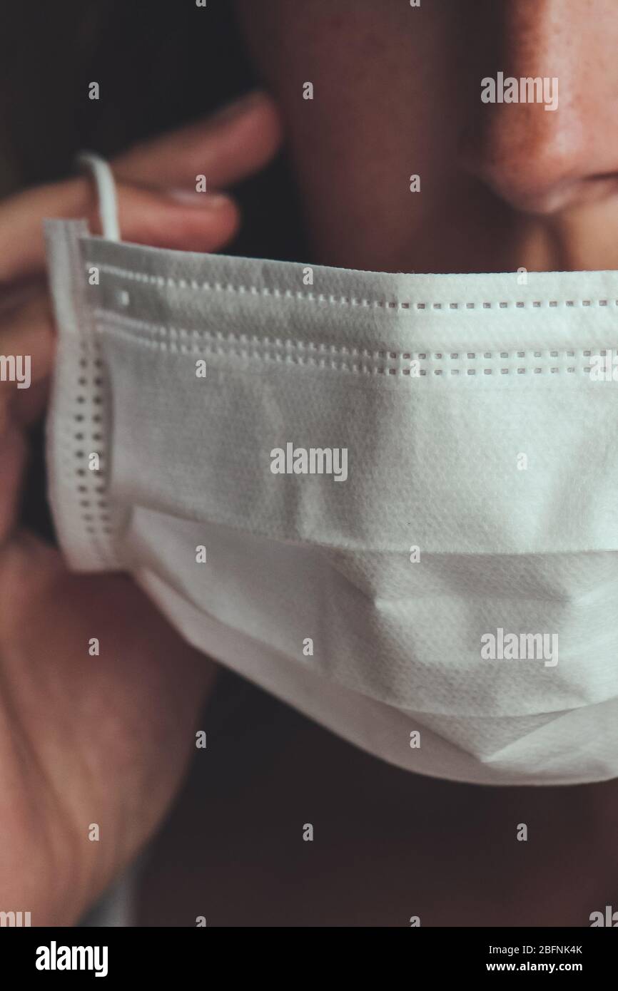 Photo détaillée d'une femme blanche non reconnaissable mettant sur un masque médical blanc pour empêcher la grippe. Fond flou, foyer sur le masque. Coronavirus, COVID-19 quarantaine. Concept de verrouillage. Banque D'Images