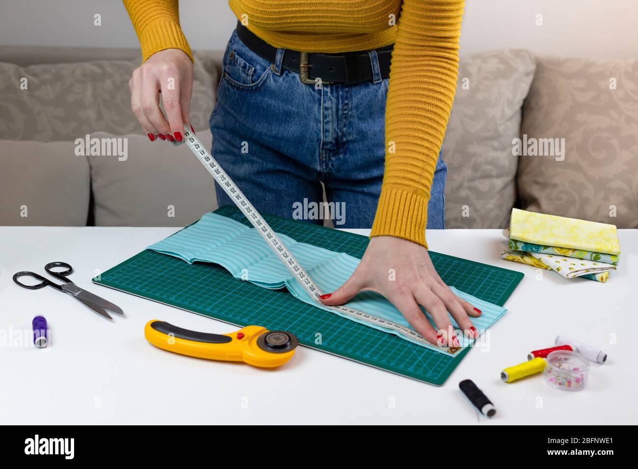 femme dans un pull jaune mesure les tissus. il y a des outils de matelassage sur la table. couteau patchwork, ciseaux, tapis de coupe doublé, auto-verrouillage, t Banque D'Images femme dans un pull jaune mesure les tissus. il y a des outils de matelassage sur la table. couteau patchwork, ciseaux, tapis de coupe doublé, auto-verrouillage, t Banque D'Images