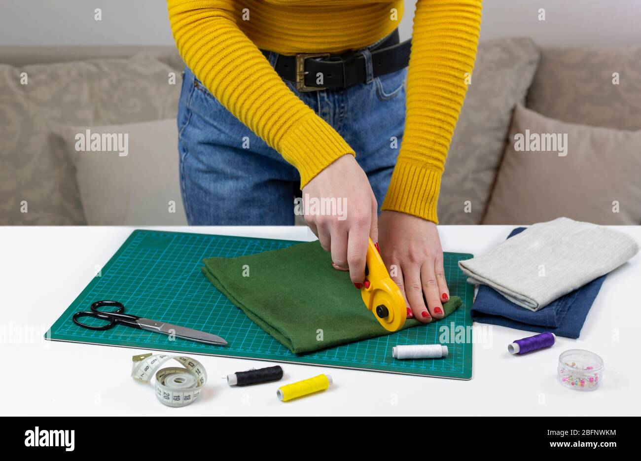 femme dans un tissu de découpe jaune. il y a des outils de courtepointes sur la table. couteau patchwork, ciseaux, tapis de coupe doublé, auto-verrouillage, filetage, centimet Banque D'Images femme dans un tissu de découpe jaune. il y a des outils de courtepointes sur la table. couteau patchwork, ciseaux, tapis de coupe doublé, auto-verrouillage, filetage, centimet Banque D'Images
