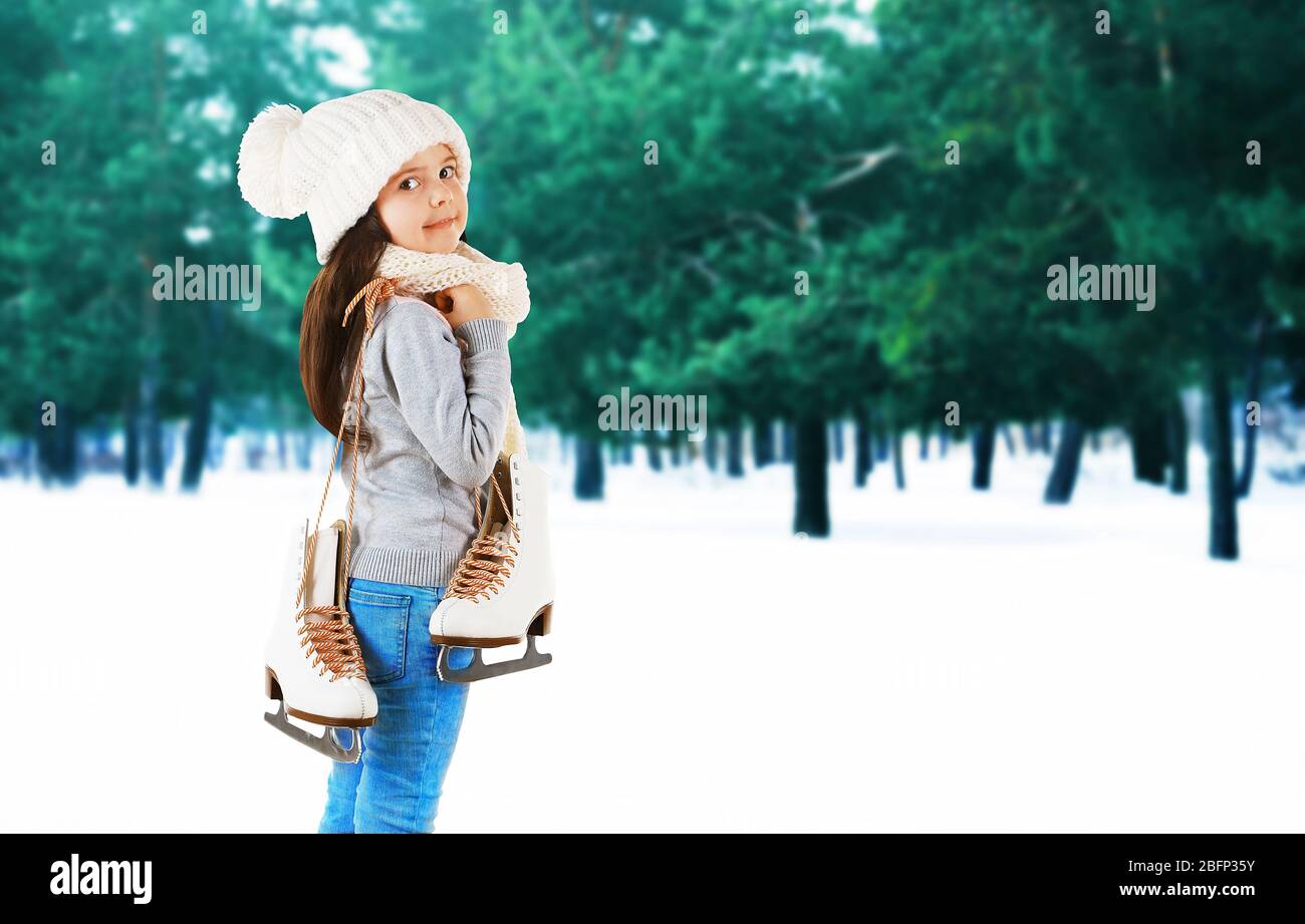 Petite fille avec patins dans des vêtements tricotés à la mode sur fond de forêt d'hiver Banque D'Images