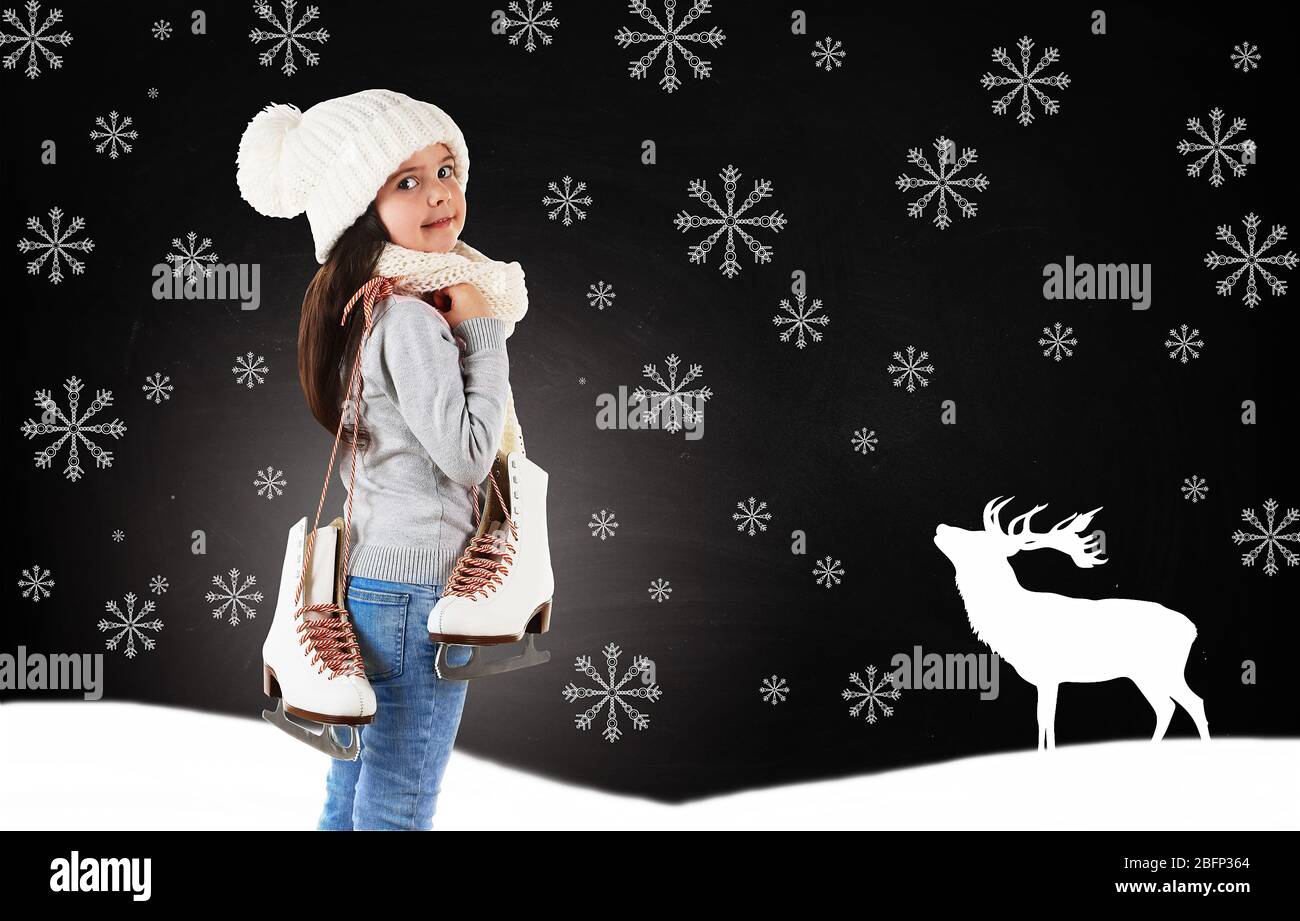 Petite fille avec patins dans des vêtements tricotés à la mode et des flocons de neige dessinés sur fond de tableau noir Banque D'Images