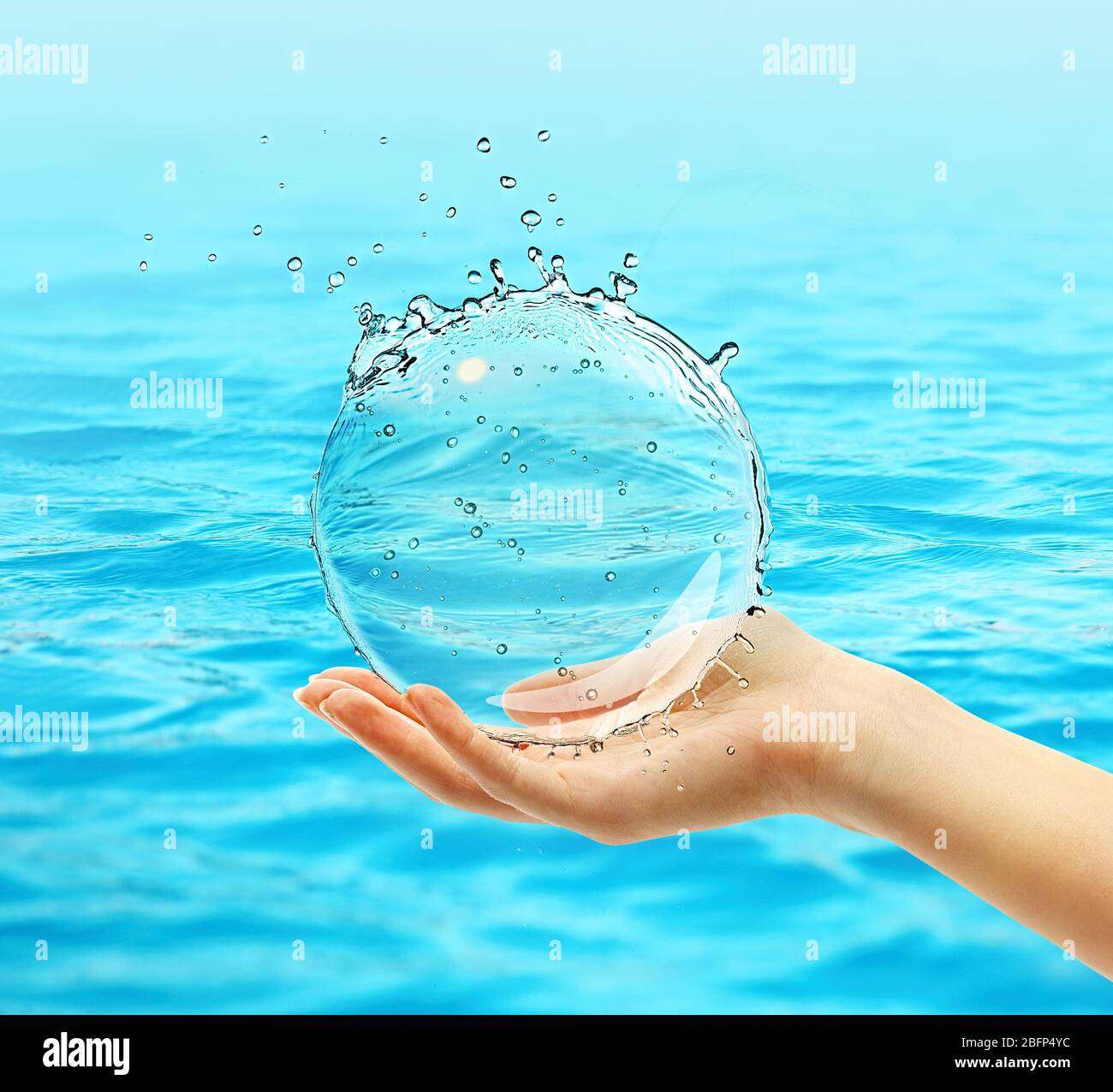 Main femelle tenant le ballon d'eau s'asperger sur fond bleu d'eau Banque D'Images