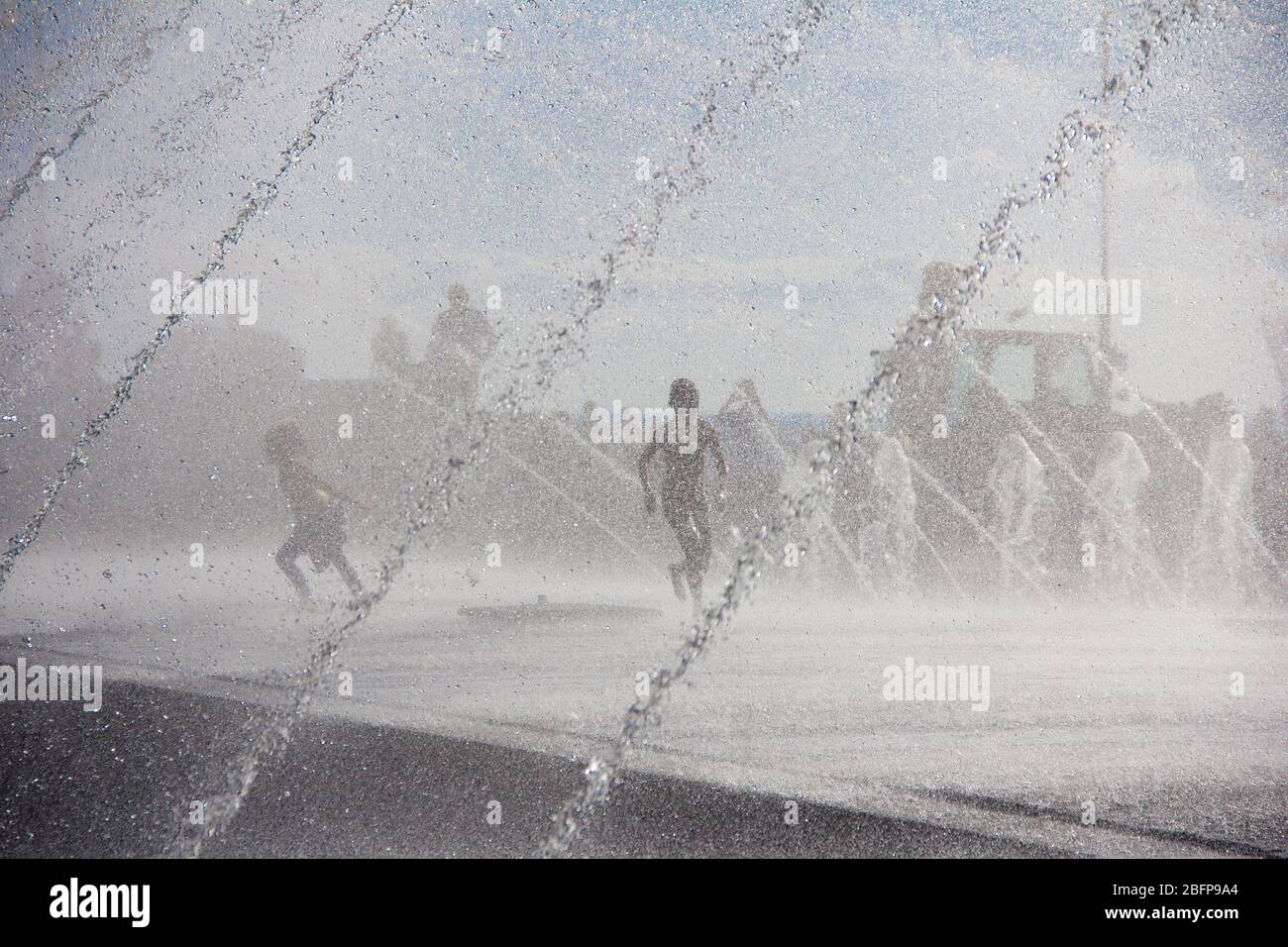 Silhouette d'enfants sautant dans l'eau fraîche de fontaine. Un garçon jouant dans des fontaines d'eau. Les enfants heureux jouant avec bonheur dans la fontaine de la ville une journée chaude Banque D'Images