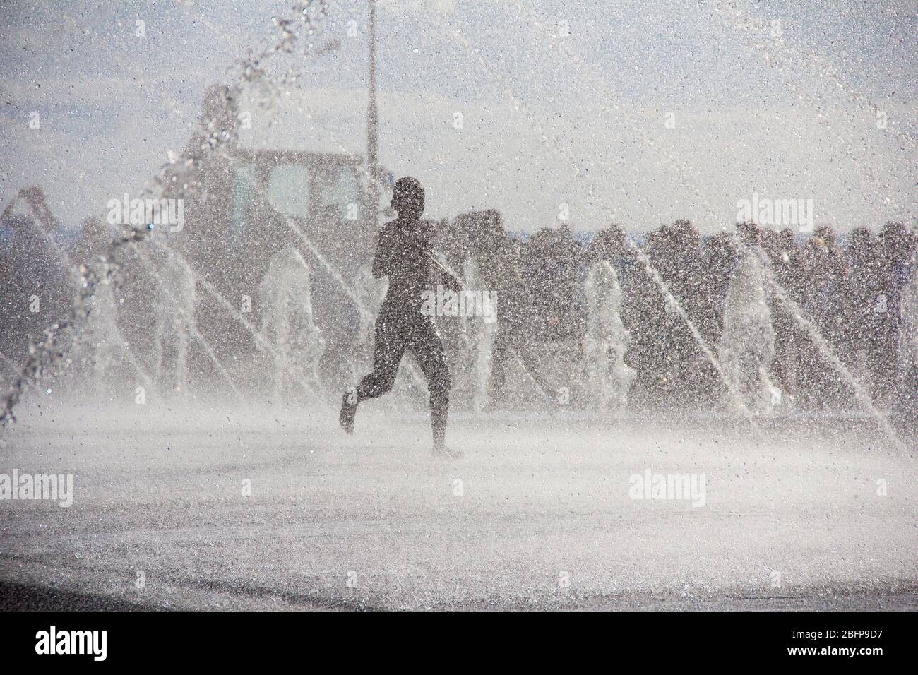 Silhouette d'enfants sautant dans l'eau fraîche de fontaine. Un garçon jouant dans des fontaines d'eau. Les enfants heureux jouant avec bonheur dans la fontaine de la ville une journée chaude Banque D'Images