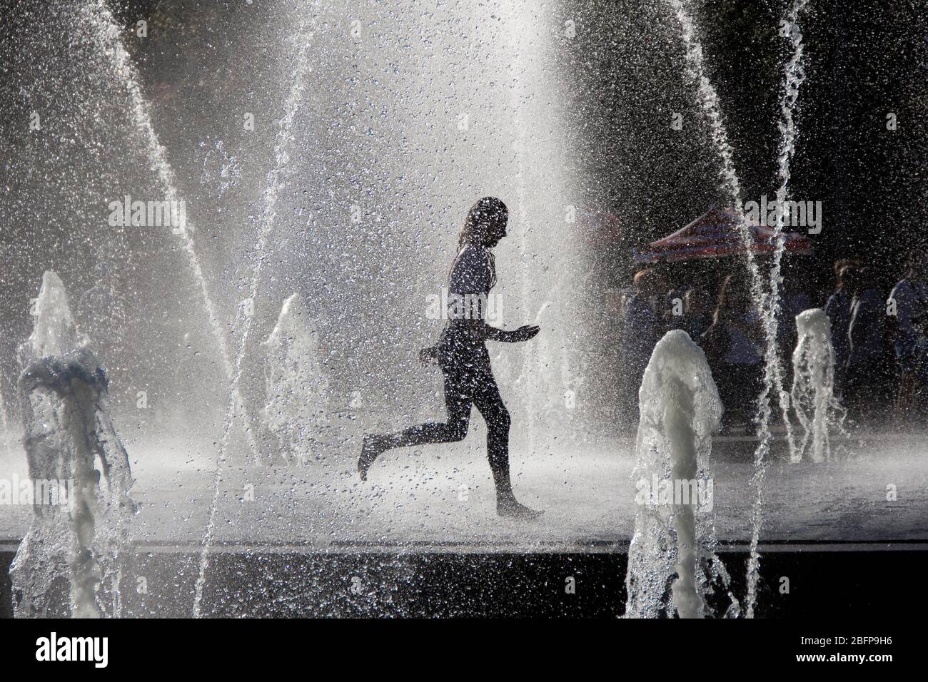 Silhouette d'enfants sautant dans l'eau fraîche de fontaine. Un garçon jouant dans des fontaines d'eau. Les enfants heureux jouant avec bonheur dans la fontaine de la ville une journée chaude Banque D'Images