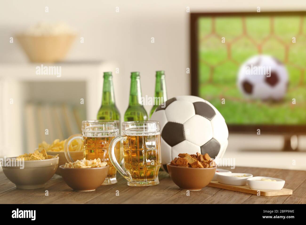 Des en-cas savoureux, de la bière et la balle sur une table de cuisine à l'arrière-plan flou Banque D'Images