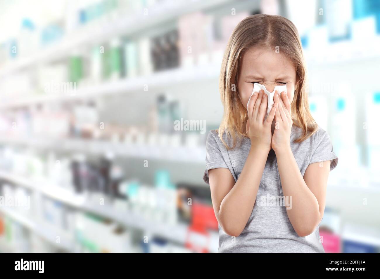 Concept d'allergies ou de froid. Petite fille soufflant nez sur tissu à la pharmacie Banque D'Images