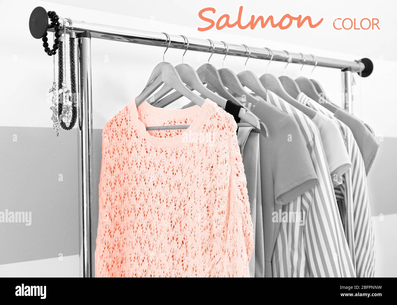 Pull de couleur saumon et autres vêtements avec accessoires élégants accrochés sur le rack au dressing Banque D'Images