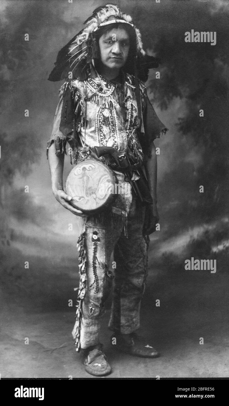 Américain indien/autochtone américain, c. 1921. Il a été identifié comme « Chef courant Deer ». Il a un revolver pistolet dans sa ceinture et un sac à franges accroché derrière son tambour joliment peint. Cette photo a été prise en Floride, États-Unis. Cet homme aurait peut-être vêtu de tous ces vêtements et accessoires merveilleusement ornés de perles pour sa famille et lui-même. Mais il est plus probable que ce fut une photo pour vendre aux touristes. Son nom a peut-être été composé juste pour le spectacle, aussi. Les touristes américains ont adoré les images amérindiennes romantiisées. Pour voir mes autres images connexes, recherchez: Prestor millésime West Banque D'Images