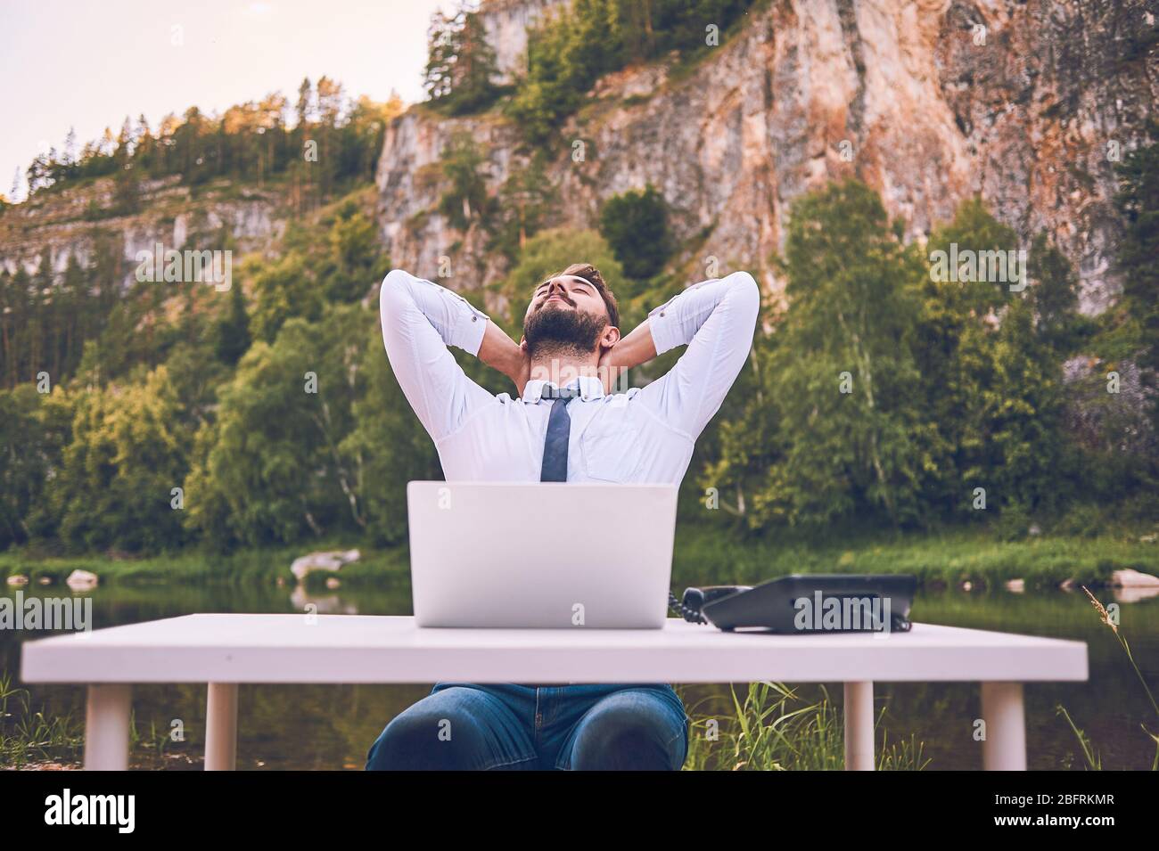 Un homme barbu travaille avec un ordinateur portable sur la nature. Un travailleur indépendant heureux est assis et utilise une application ou un site Web sur l'herbe. Travailler à distance en soi Banque D'Images