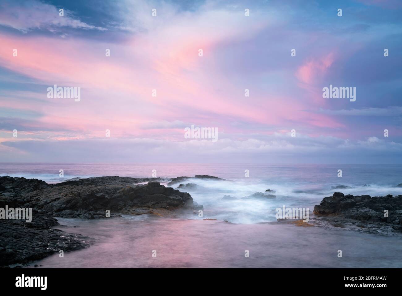 Les couleurs du lever du soleil illuminent le ciel sur le littoral de lave au parc de la plage de Kohanaiki le long de la côte de Kona sur la Grande île d'Hawaï. Banque D'Images