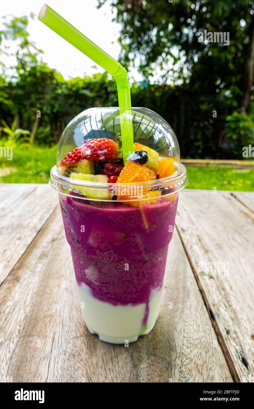 Fruits mélangés juteux et doux dans une tasse en plastique transparent sur une table en bois. Banque D'Images