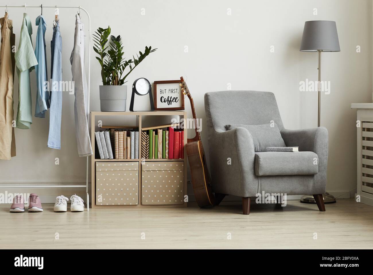 Vue sur toute la longueur de l'intérieur de l'appartement studio avec un design minimaliste, foyer sur un fauteuil gris confortable et un porte-vêtements contre le mur blanc, espace de copie Banque D'Images