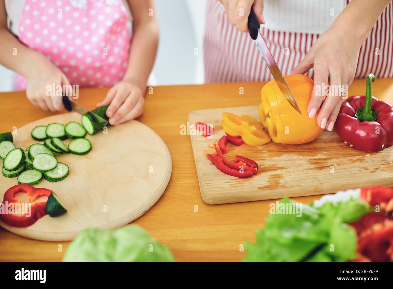 Sans visage. Les mains familiales préparent une salade de légumes frais sur la table dans la cuisine. Banque D'Images