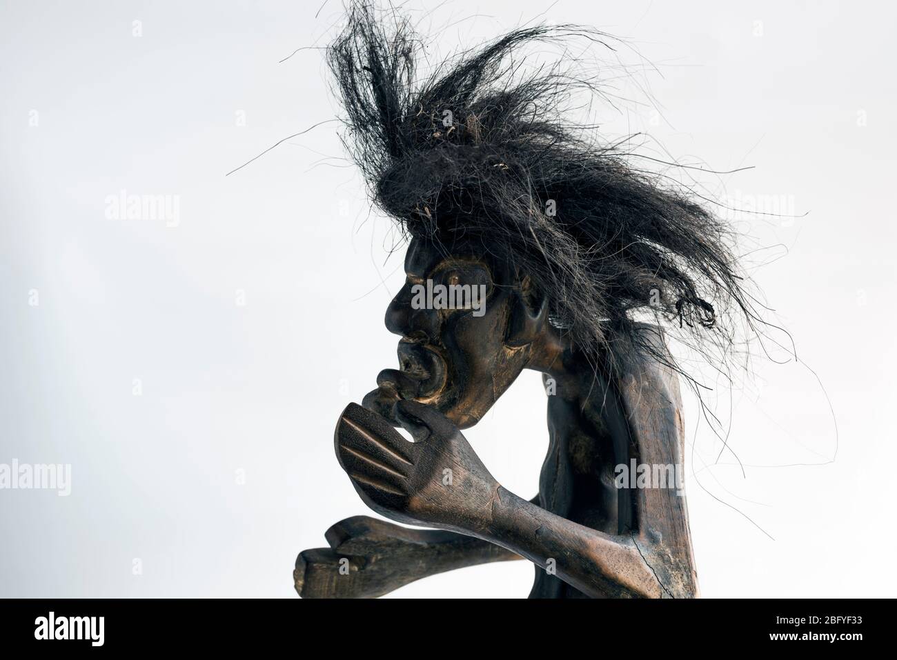 Figure sculptée en bois d'un homme primitif portant une jupe en paille et de longs cheveux cousés noirs. Concept; mauvais jour de cheveux, différence, natif, sauvage, unkempt, effrayant. Banque D'Images