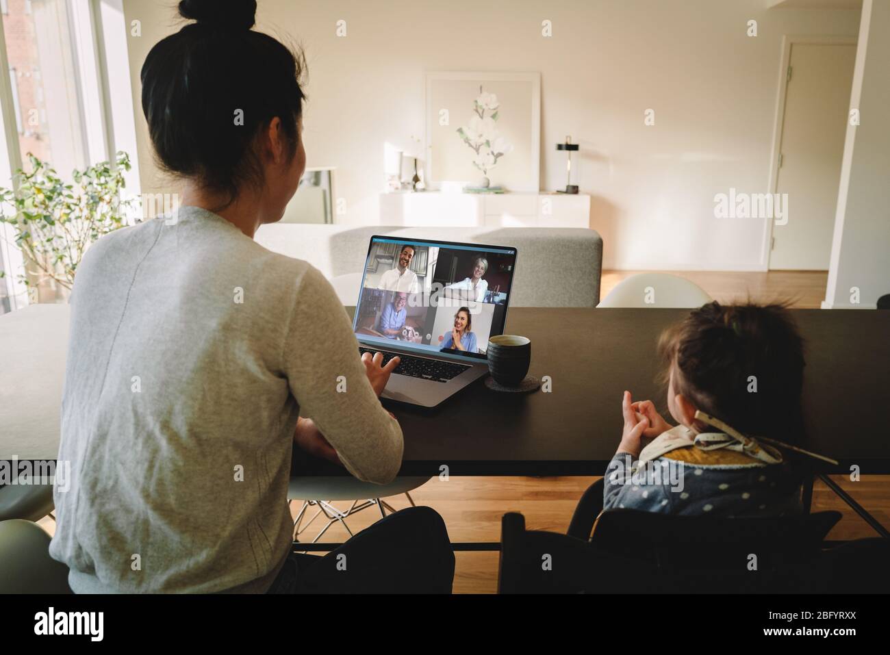 Femme travaillant à la maison, avec sa fille assise à la table, ayant une conférence vidéo. Femme d'affaires ayant une conférence vidéo de Banque D'Images