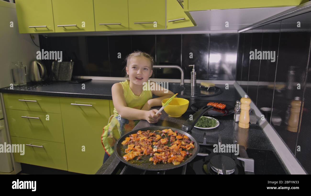 Une fille intelligente qui apprend à cuisiner. Jeunes enfants maltraités pour faire cuire une omelette sautée aux œufs napolitains à partir de saucisses d'afumicato. Faites frire la tomate et la saucisse. Banque D'Images