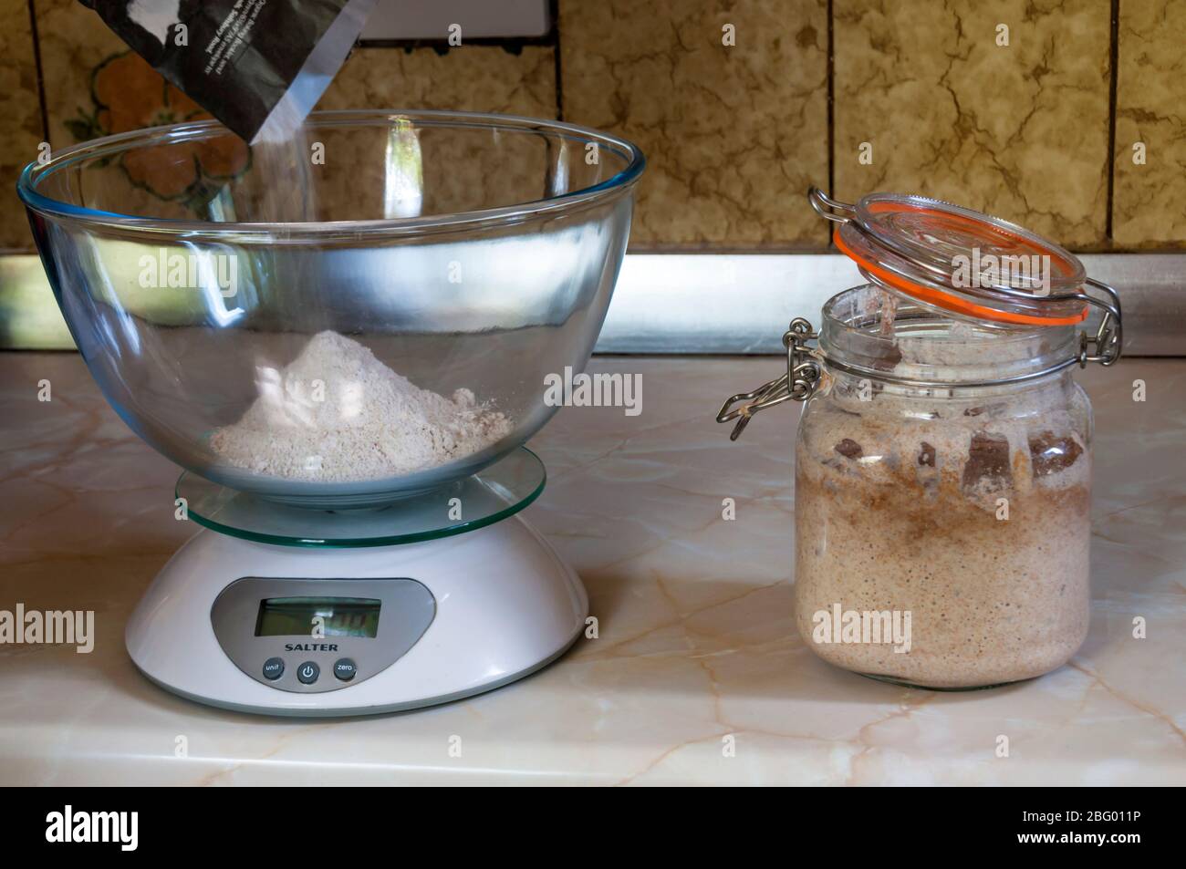Peser la farine prête à faire du pain au levain avec le levain activé dans un bocal en verre. Banque D'Images