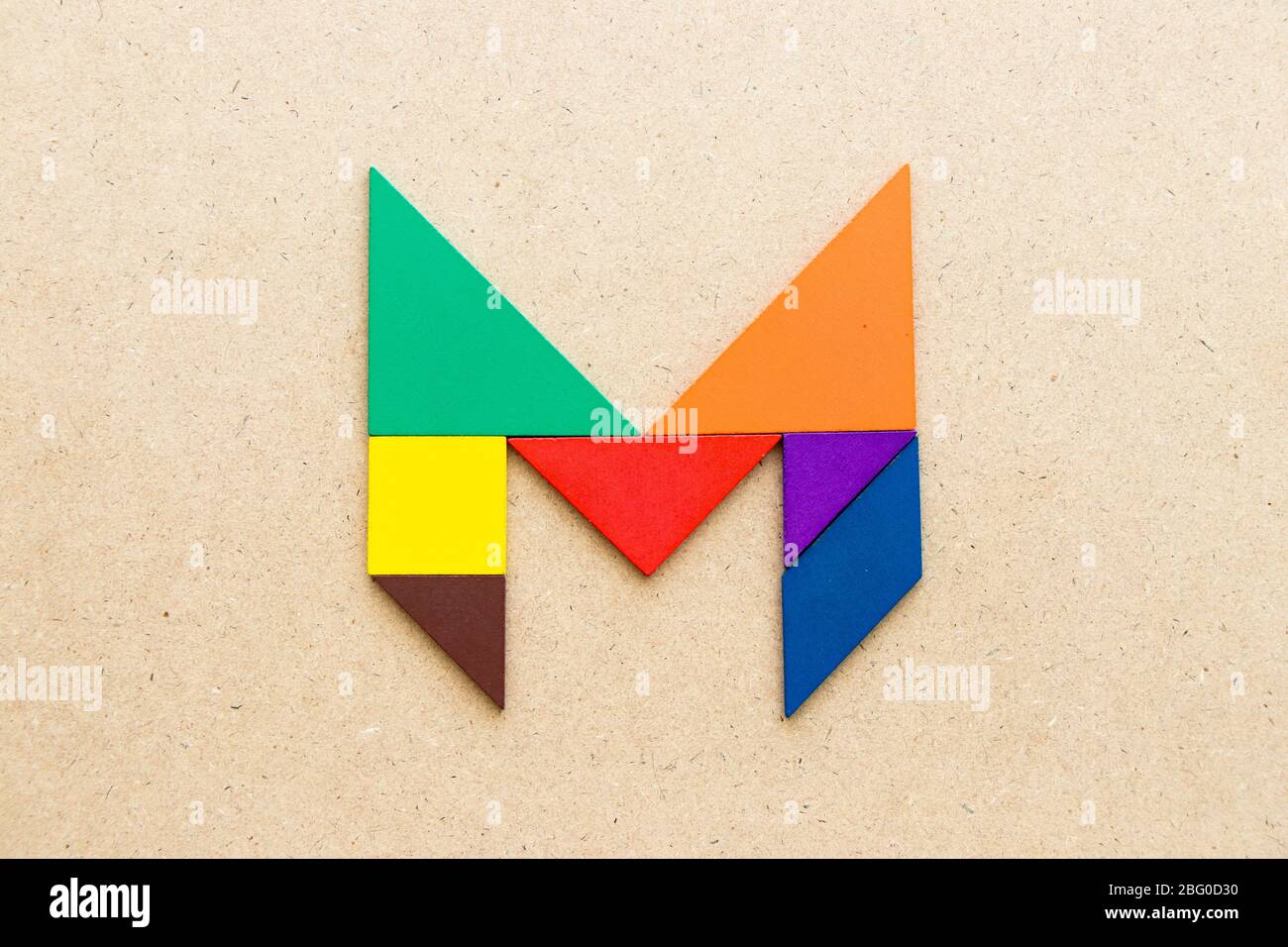 Puzzle en forme de lettre M en forme de tangram sur fond de bois Banque D'Images