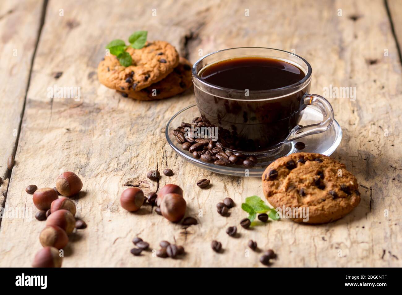 Café noir dans une tasse de verre avec des grains de café. Près des cookies et des noisettes Banque D'Images