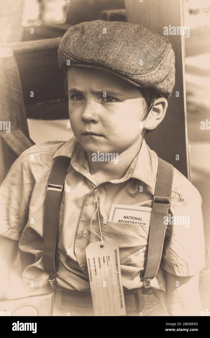 Portrait sépia à l'ancienne d'un garçon évacué en casquette plate et  bretelles, à l'aspect malheureux de la gare d'époque, événement d'été de la  seconde guerre mondiale des années 1940, Royaume-Uni Photo Stock -
