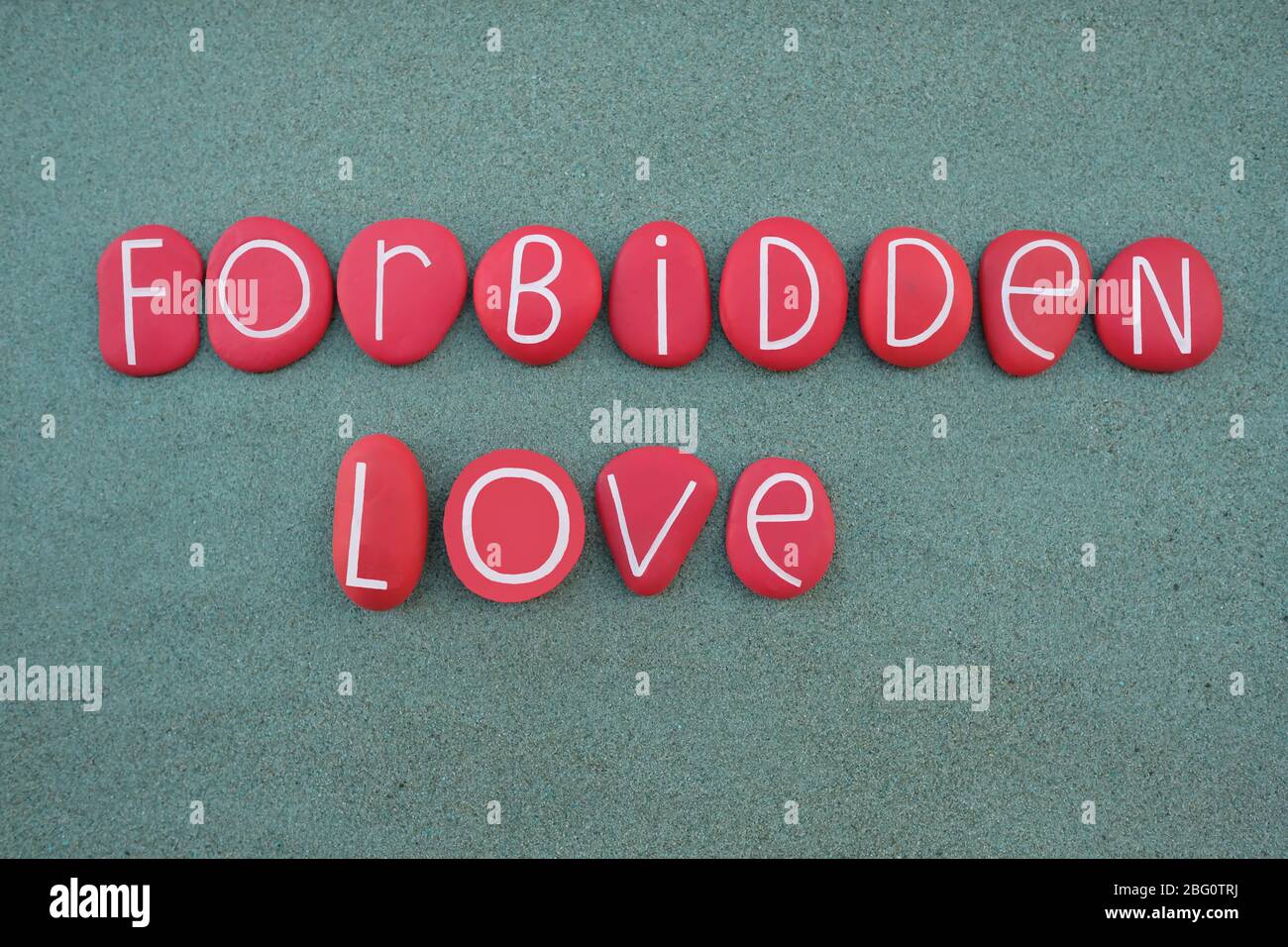 Amour interdit, texte créatif composé de lettres en pierre de couleur rouge sur sable vert Banque D'Images